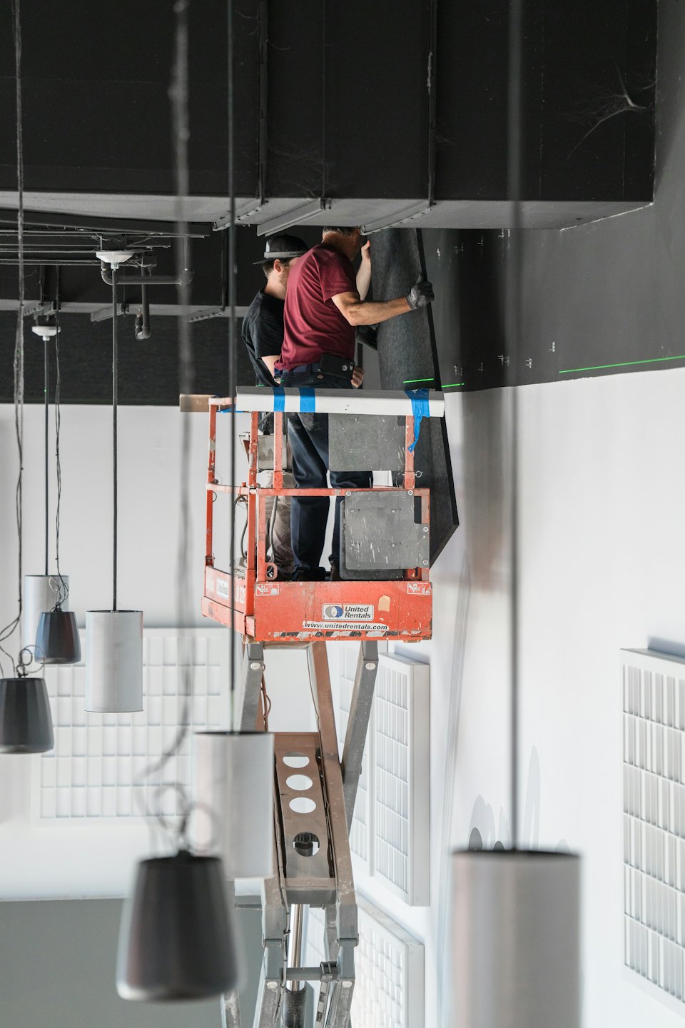 Men installing a dark panel on a black wall from a scissor lift.