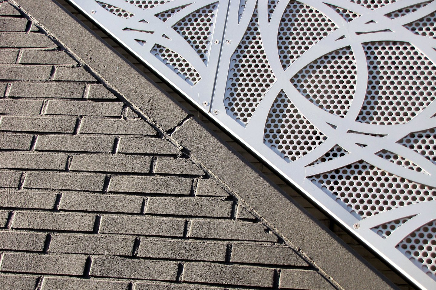 Grey brick wall meets a perforated metal panel on a building.